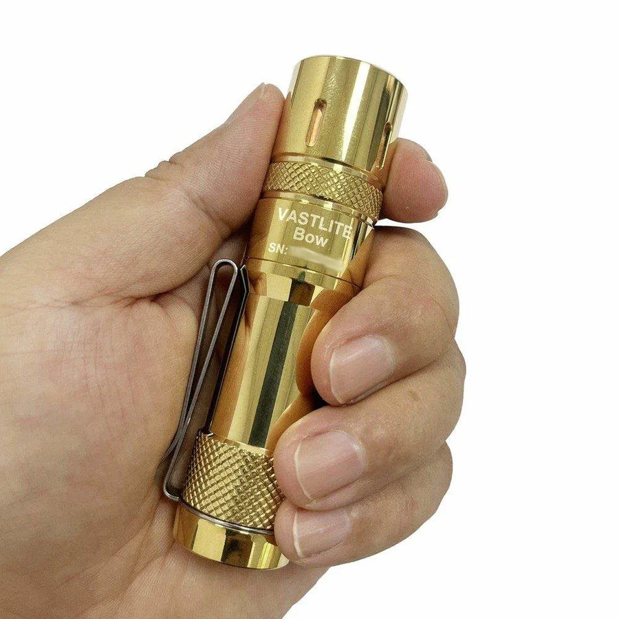 Brass Vastlite flashlight held in a hand against a white background