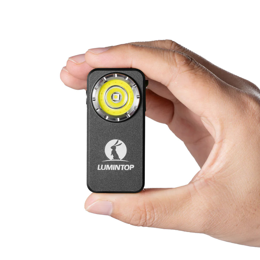 Hand holding a small black flashlight with yellow center and 'Lumintop' branding on a white background