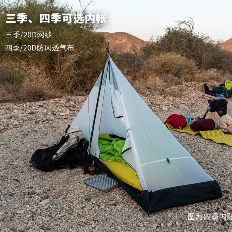 Single-person tent set up in a desert-like environment with camping gear around.