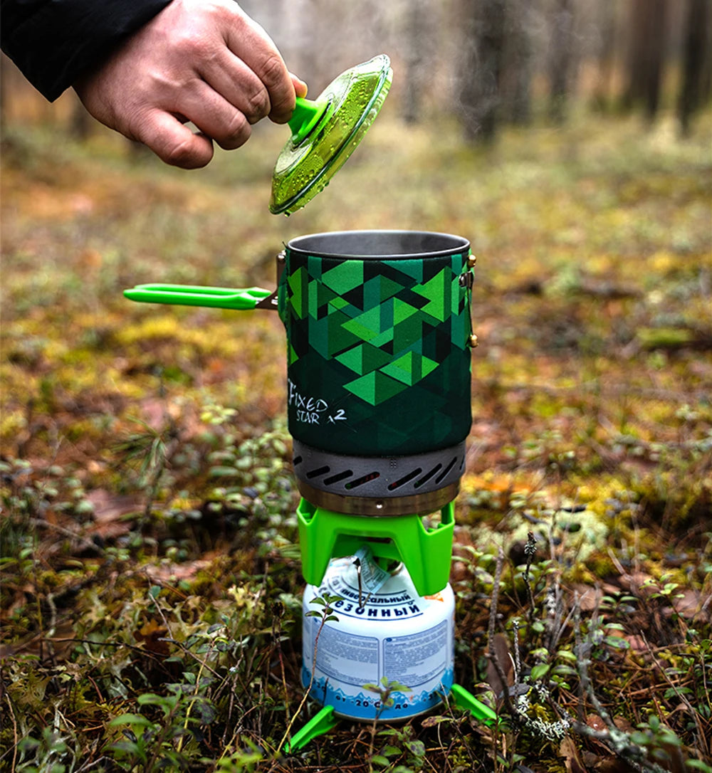 Person using a portable camping stove with a green geometric pattern in a forest setting.