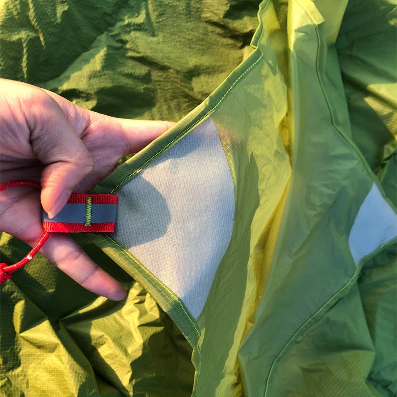 Close-up of a hand holding a red and blue tag inside a green fabric