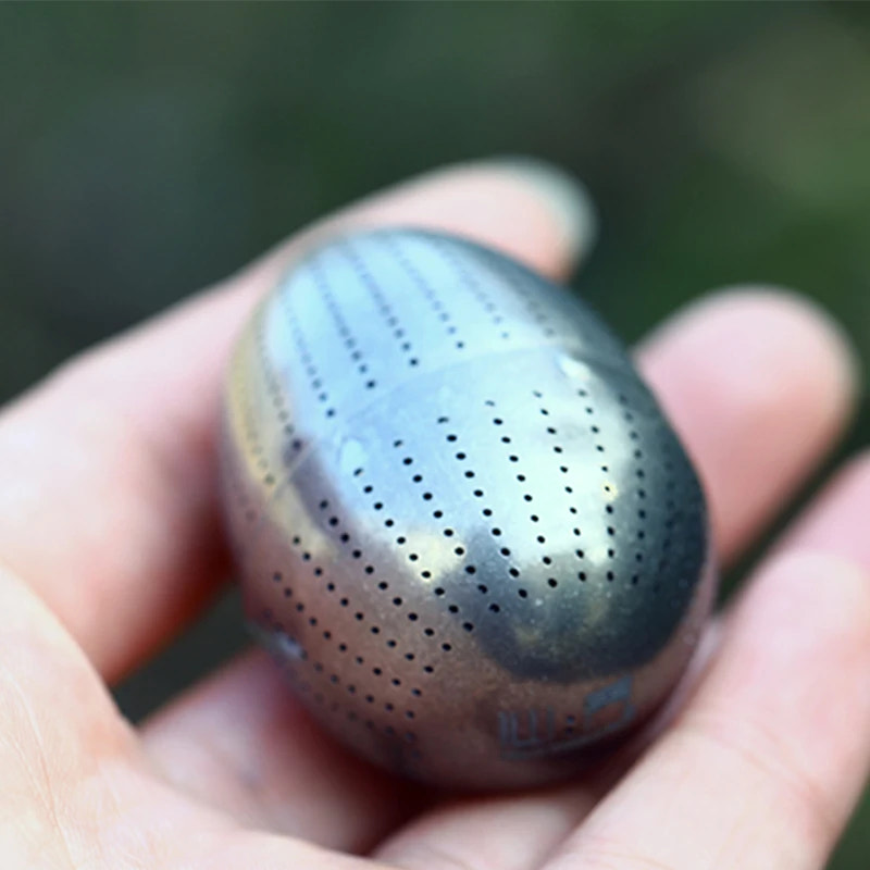 Tea strainer held in a hand with a blurred green background