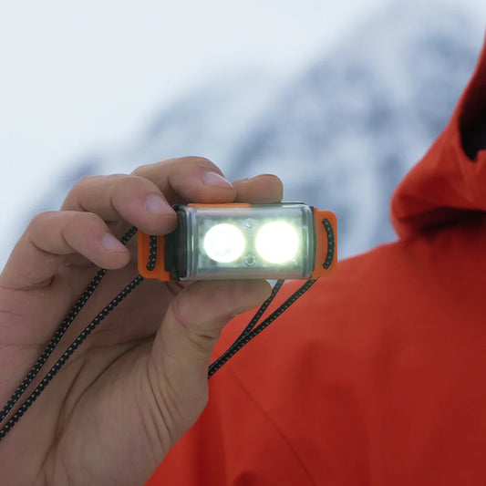 Hand holding a small flashlight with a blurred snowy landscape in the background