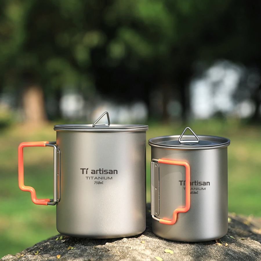 Two titanium mugs with orange handles on a natural background