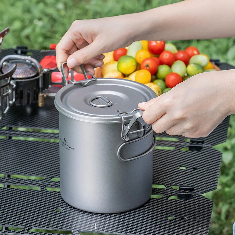 Person opening a camping pot with a campfire and fruits in the background