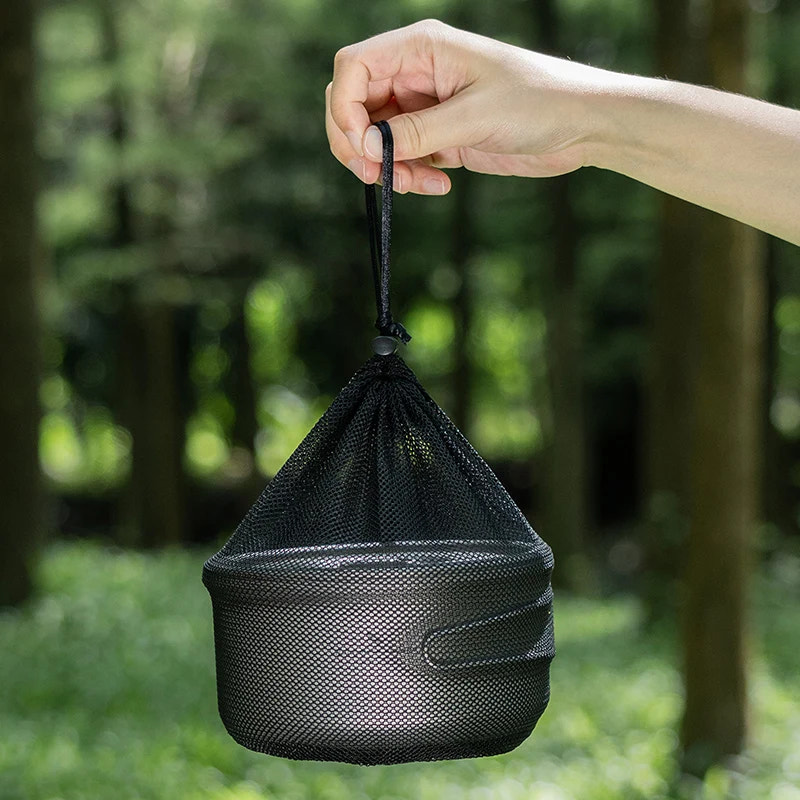 Black mesh bag held by a hand with a blurred green forest background