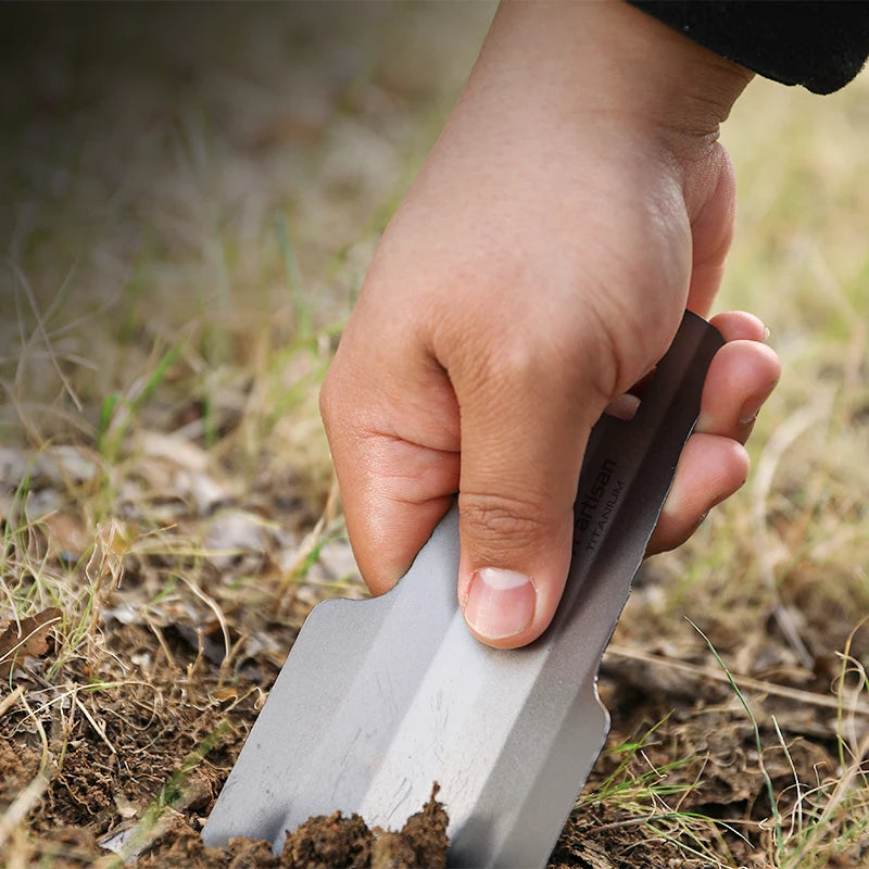 Hand using a small gardening tool in soil with a blurred natural background
