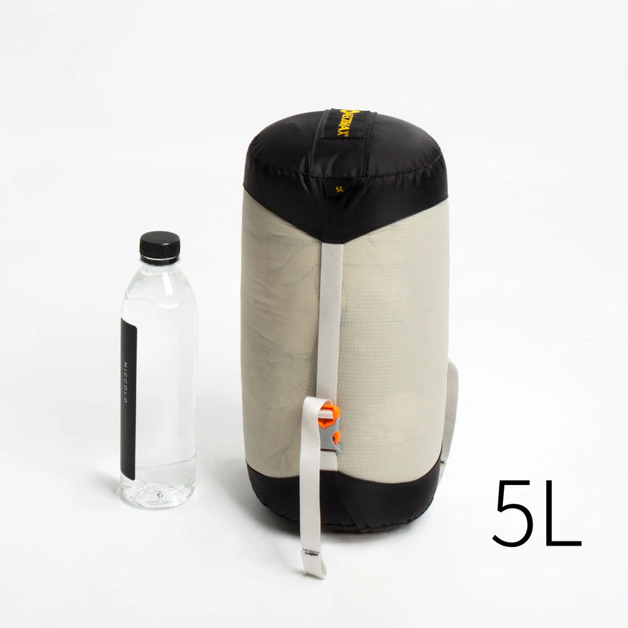 Small black and beige compression sack with a water bottle for scale on a white background
