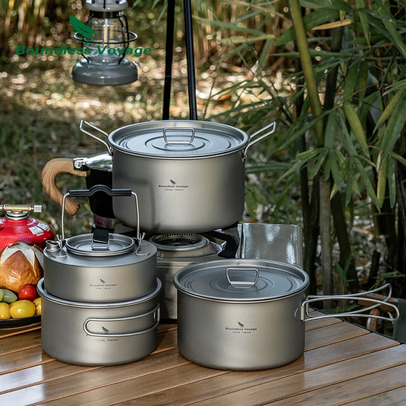 Set of camping cookware on a wooden table with a lantern and food items in the background.