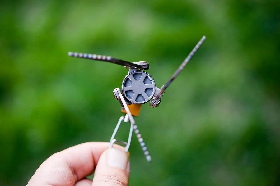 Hand holding a camping stove against a blurred green background