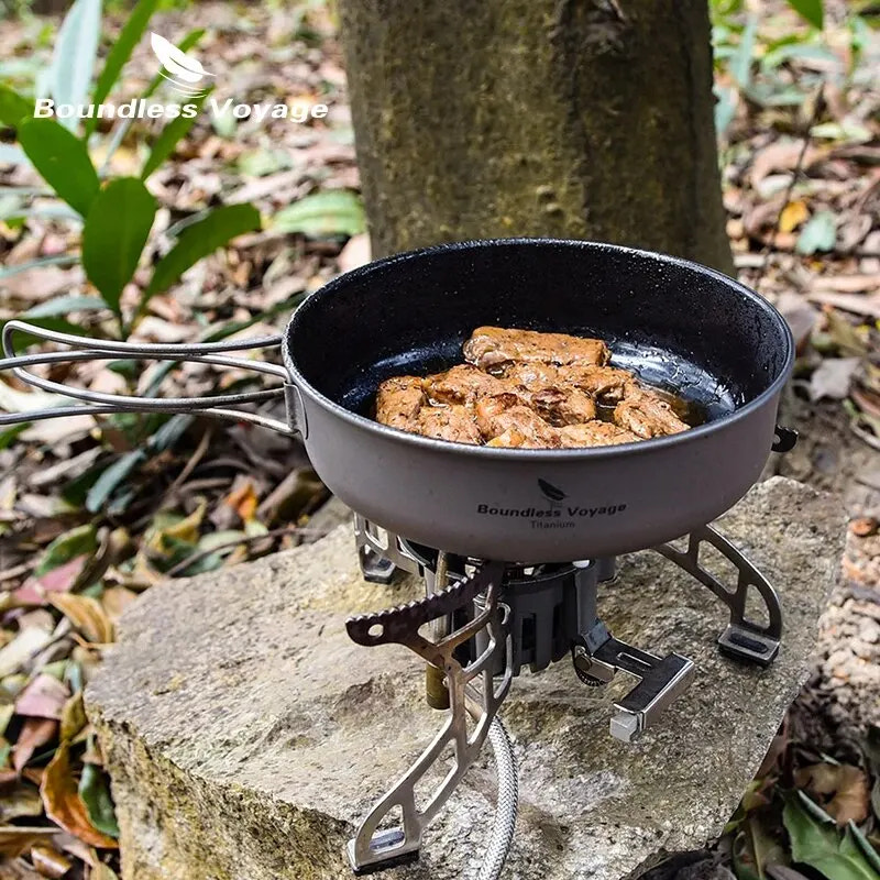 Portable stove with a frying pan containing food on a rock in a natural setting, featuring 'Boundless Voyage' branding.