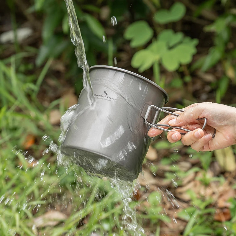 Person washing a titanium camping pot into a natural setting