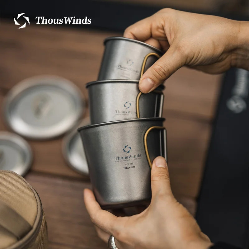 Stack of ThousWinds titanium cups held by a person on a wooden surface.