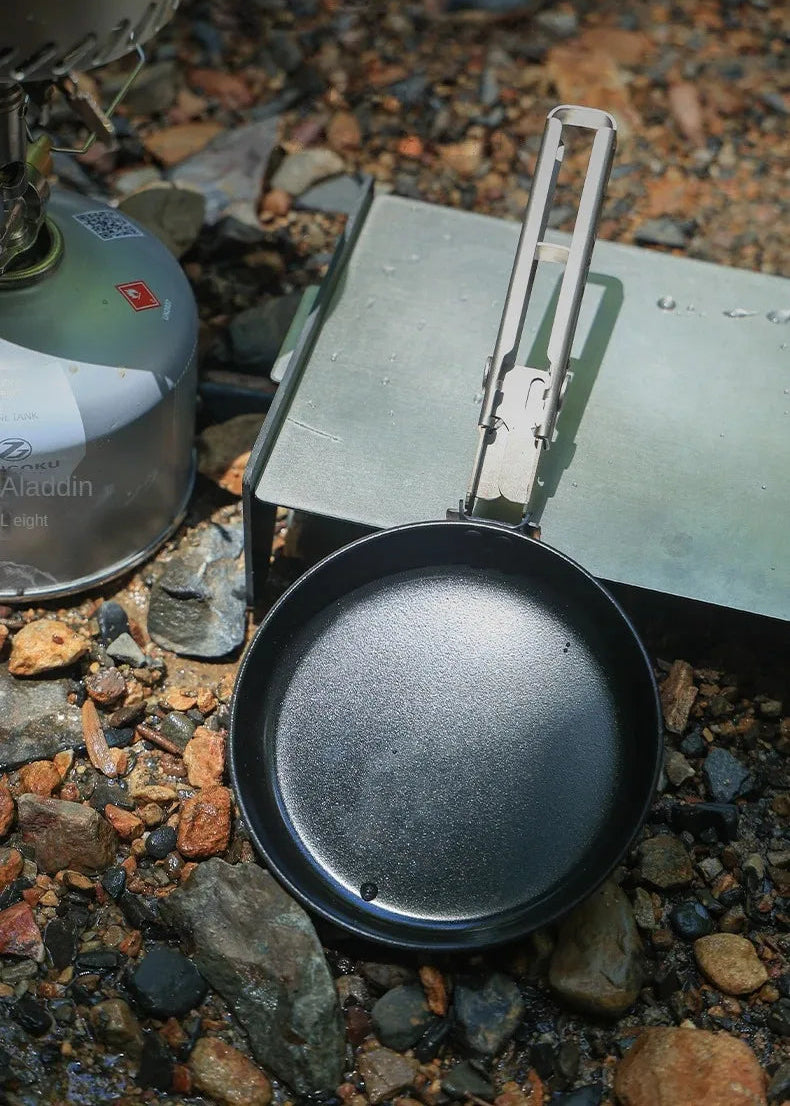 Black frying pan on a camping stove with a blurred natural background