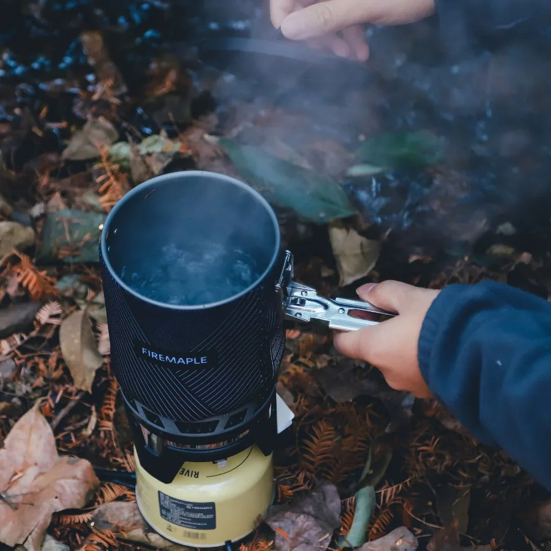 Person using a Firemaple camping stove outdoors with smoke rising.
