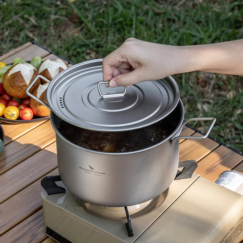 Titanium pot on a camping stove with a hand closing the lid, outdoors.