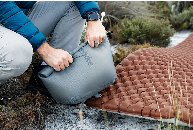 Person setting up a camping mat outdoors with a visible brand logo.