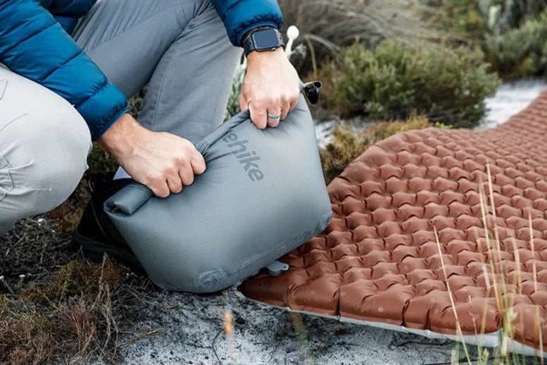 Person setting up a camping mat outdoors with a visible brand logo.