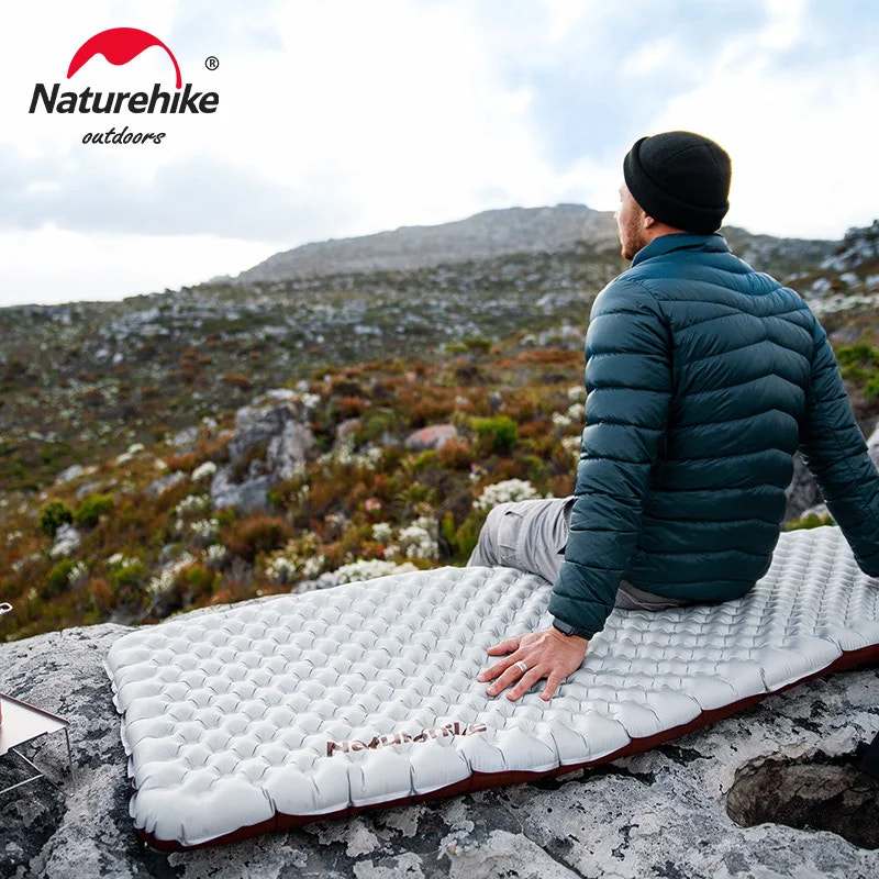 Person sitting on a Naturehike outdoor mat in a mountainous landscape
