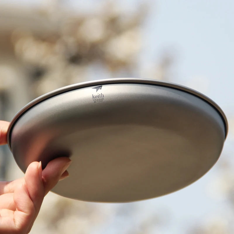 Person holding a metallic bowl with 'Keith' branding against a blurred natural background