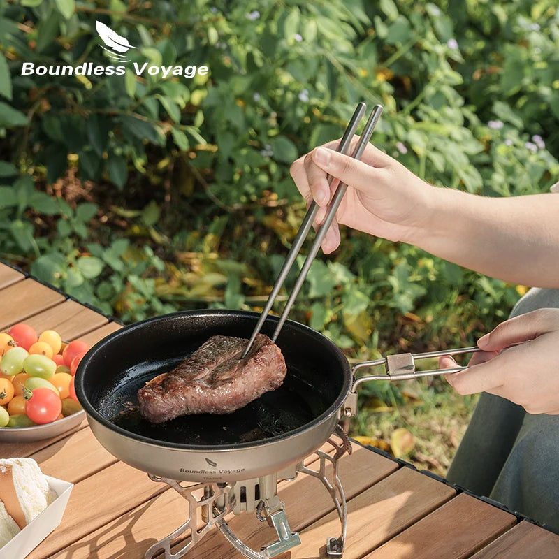 Person grilling a steak on a portable stove with 'Boundless Voyage' branding, outdoors.