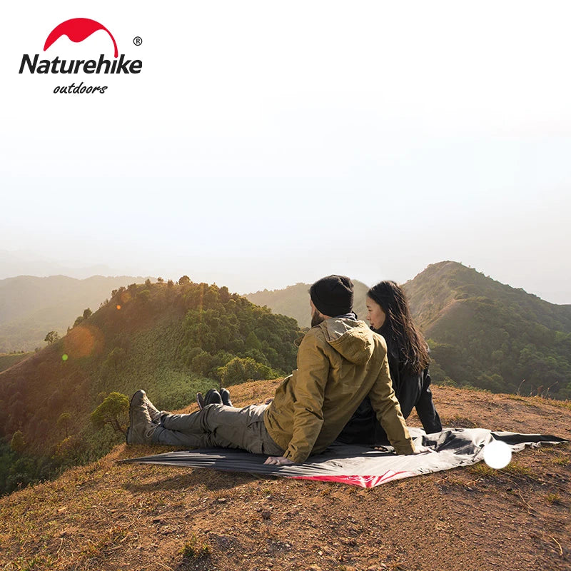 Two people sitting on a Naturehike branded blanket in a mountainous landscape.