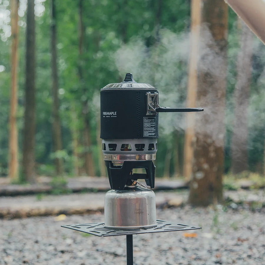 Portable camping stove with steam rising in a forest setting
