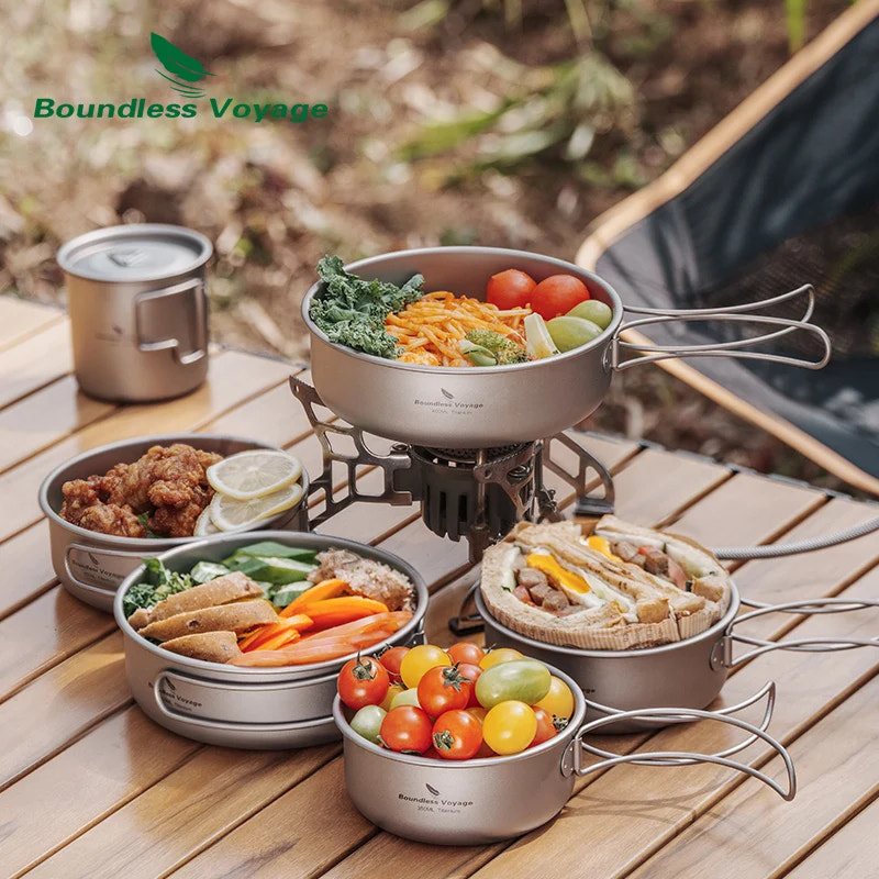 Camping cookware set with food on a wooden table outdoors, featuring 'Boundless Voyage' brand.