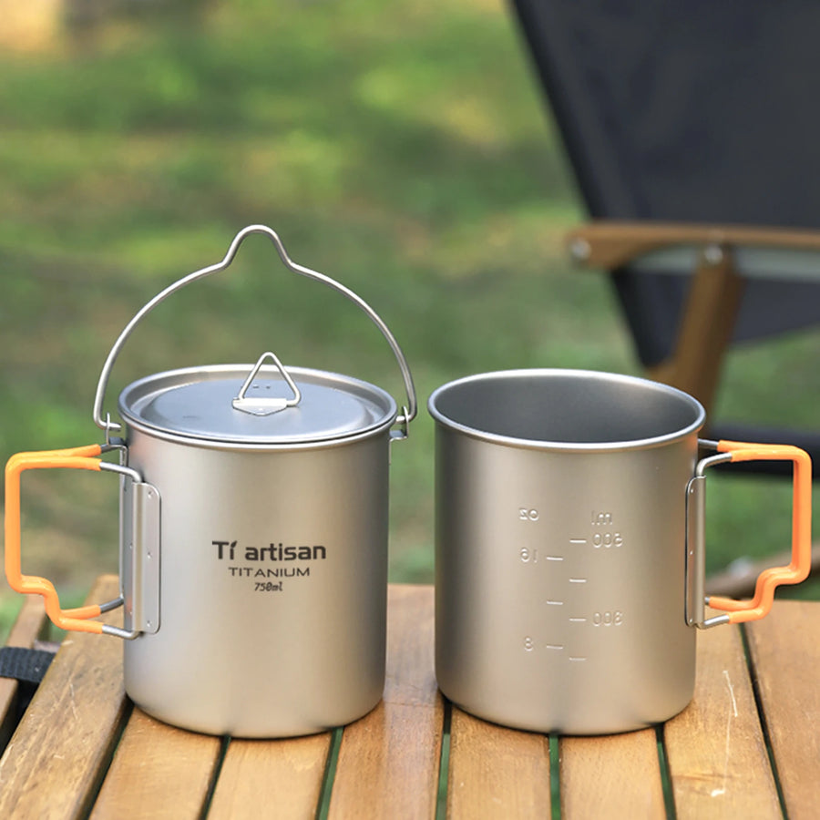 Two titanium mugs with handles on a wooden surface outdoors.
