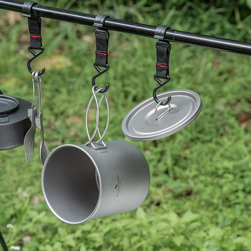 Camping pots and utensils hanging from a rod with a grassy background