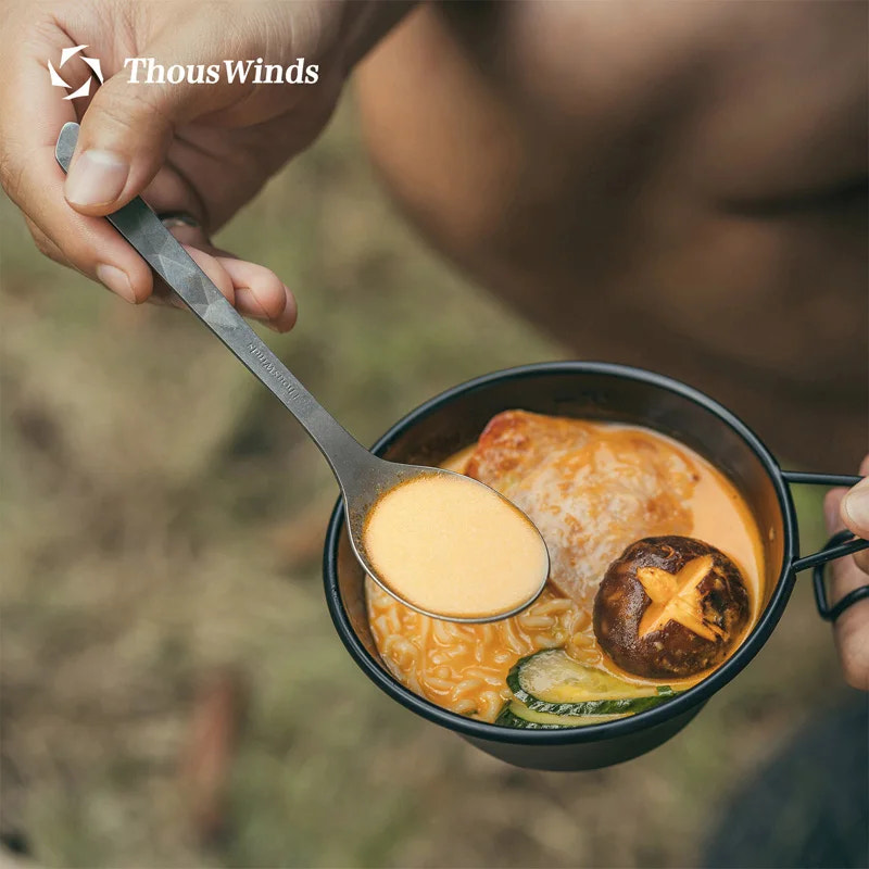 Person holding a spoon over a bowl of soup with a blurred background