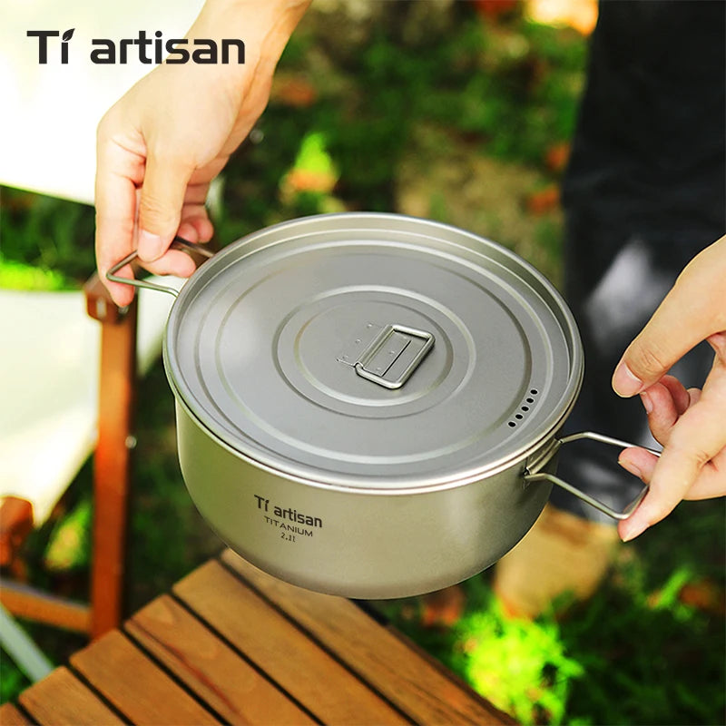 Titanium cookware with lid held by a person outdoors, featuring Tiartisan branding.