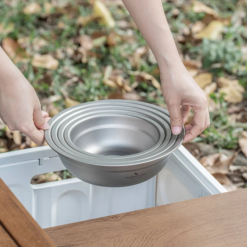 Person holding a stack of metal bowls outdoors with grass and leaves in the background