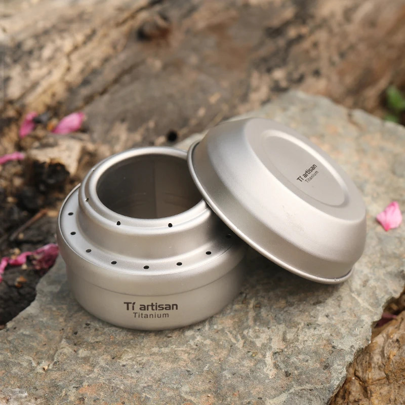 Titanium container with lid on a rocky surface, featuring 'Ti artisan' branding.