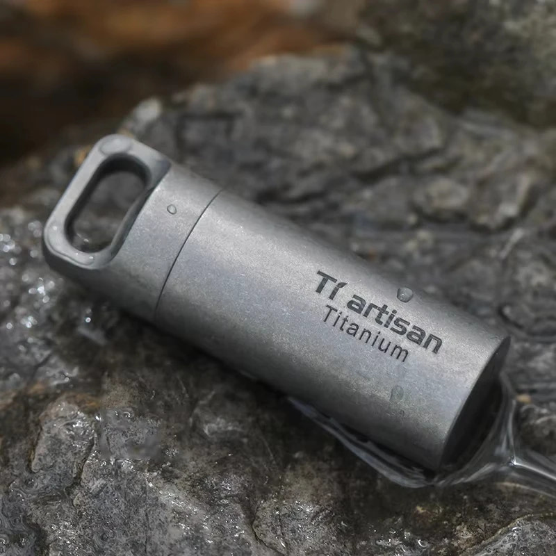 Titanium vial with 'Ti artisan Titanium' branding on a rocky surface