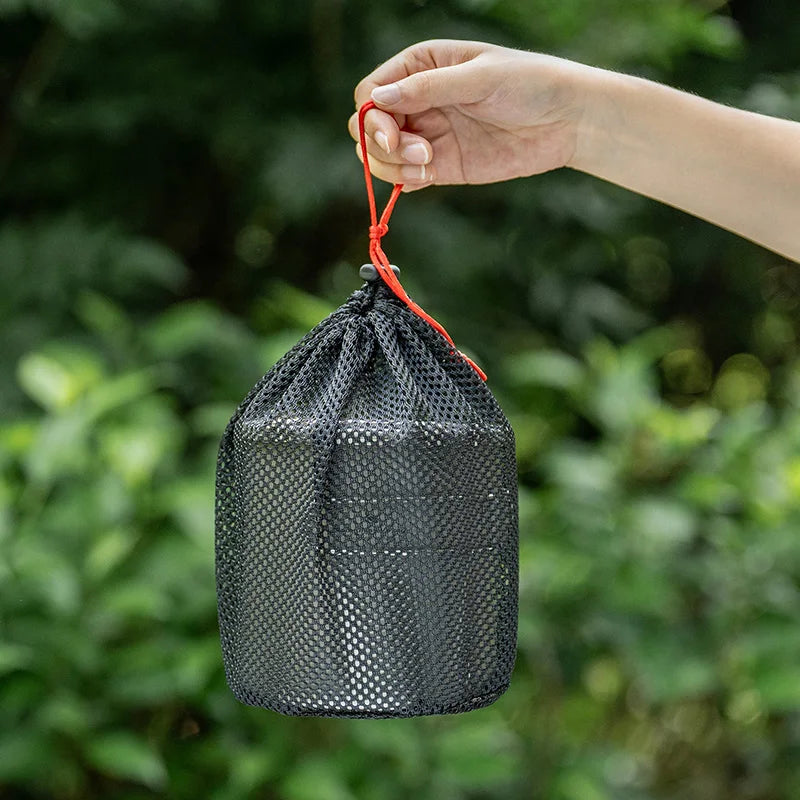 Black mesh drawstring bag held by a hand with a blurred green background