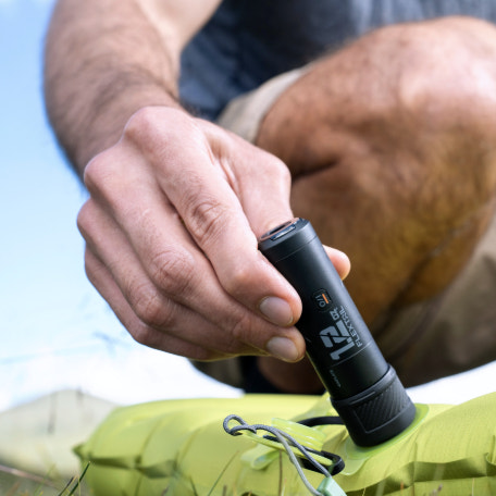 Person holding a black electronic device with "Flextail" branding on a green surface.
