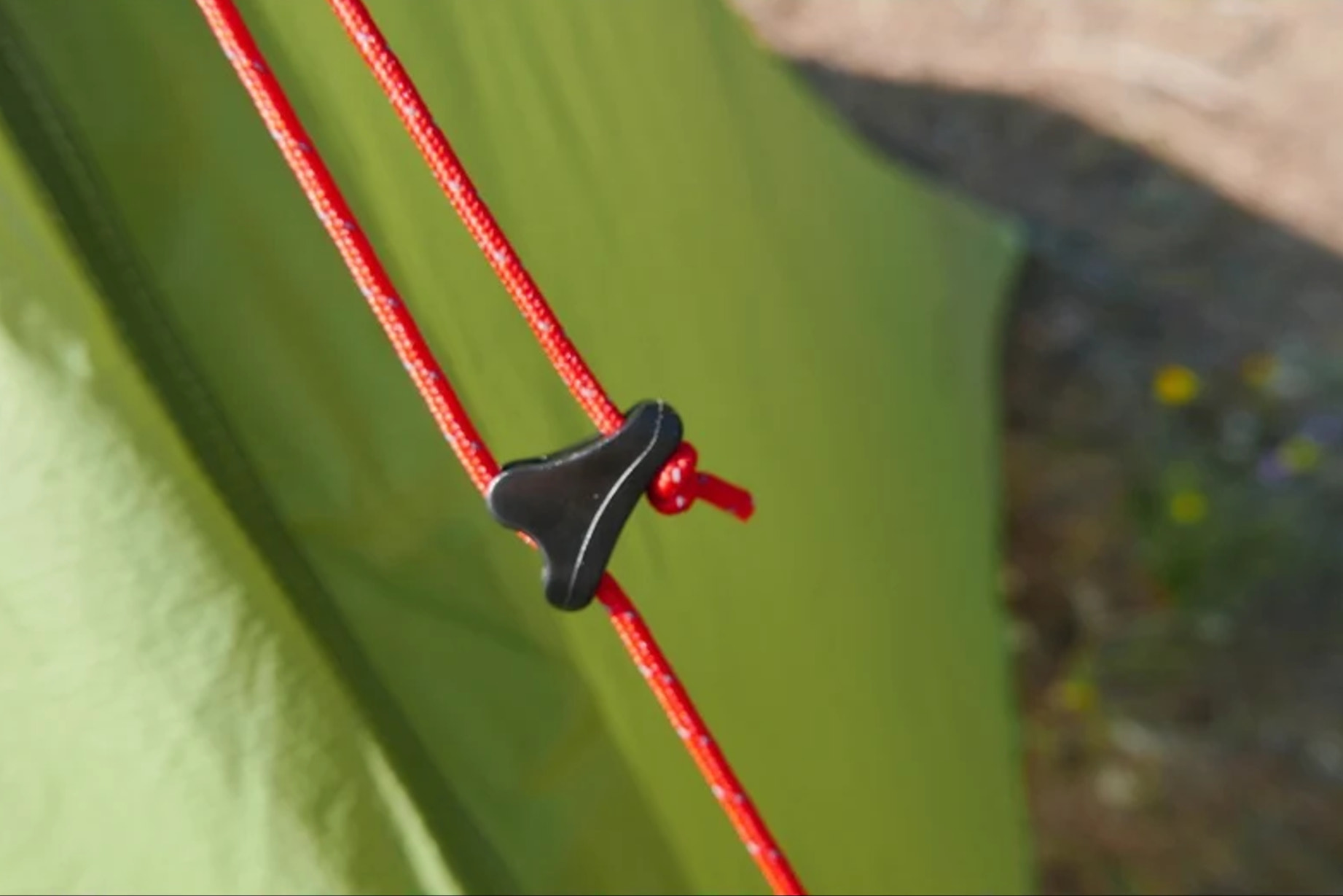 Close-up of a green tent with red ropes and black plastic knotter.
