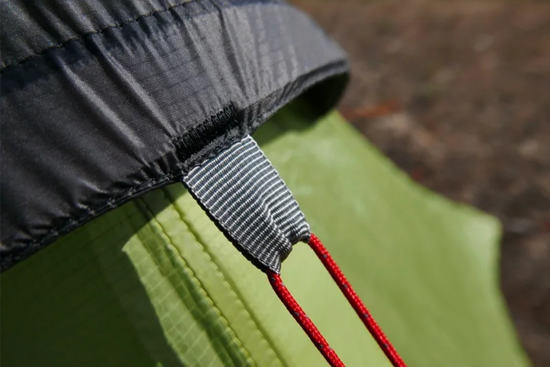 Close-up of a tent zipper with red pull tab on a green and black tent fabric.