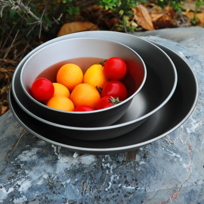 Set of titanium bowls with colorful fruits on a stone surface