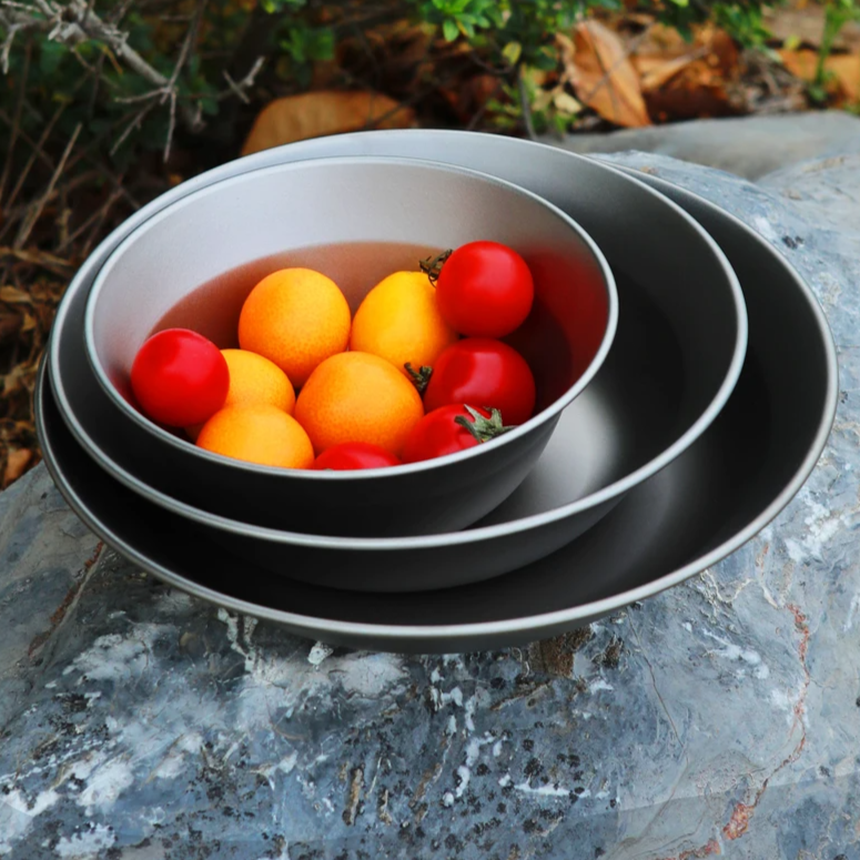 Set of titanium bowls with colorful fruits on a stone surface