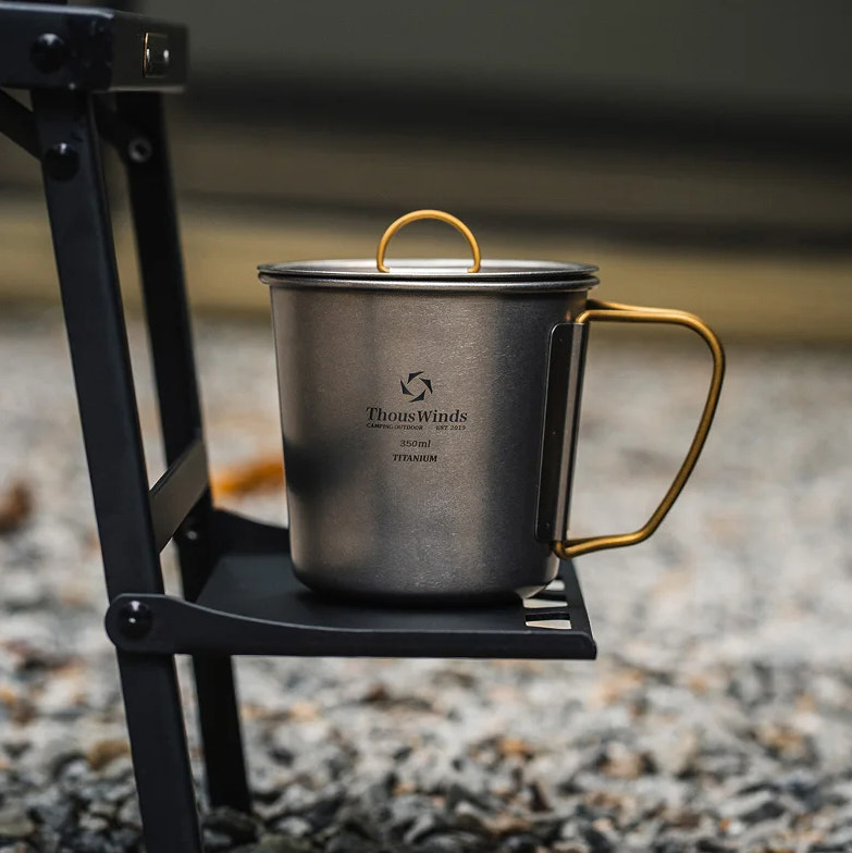titanium mug with gold handle on a black metal stand outdoors