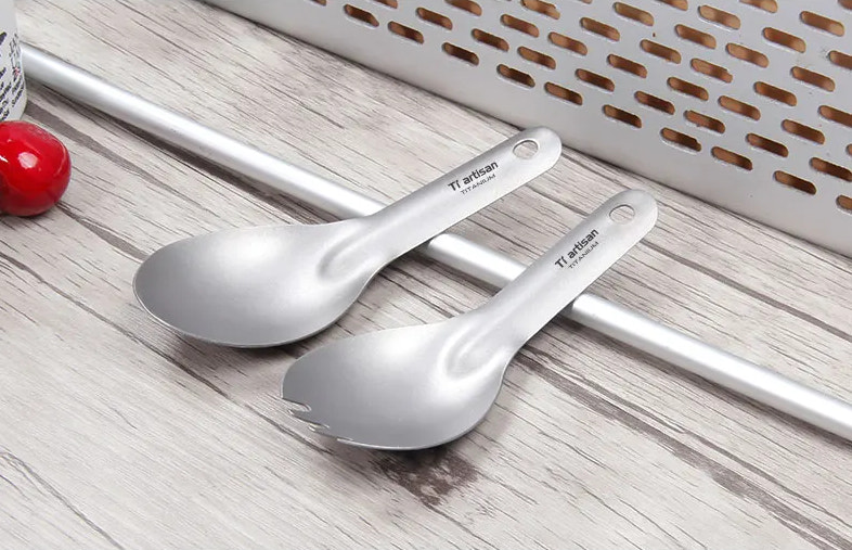 Two titanium spoons on a wooden surface with a white basket in the background.