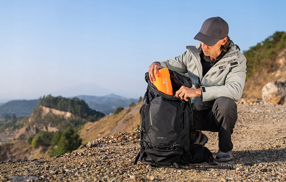 Person sitting outdoors, unpacking a backpack on a rocky terrain with mountains in the background.