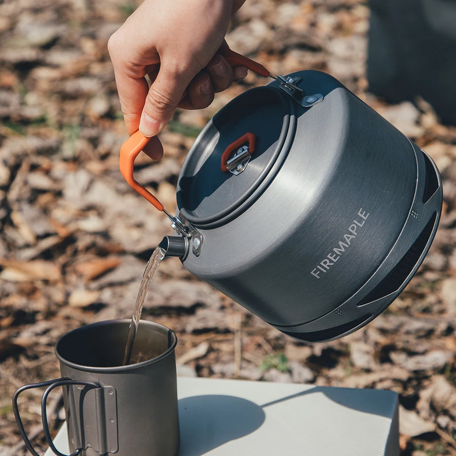 Person pouring water from a Firemaple camping kettle into a mug outdoors.