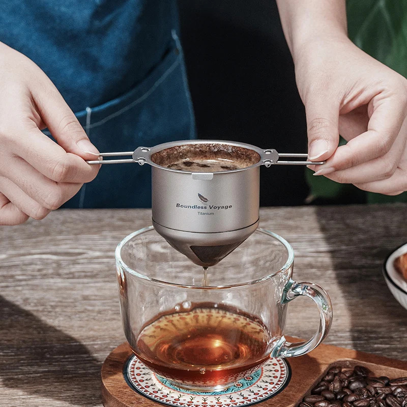 Person using a Titanium coffee filter to make tea in a glass mug on a wooden table.