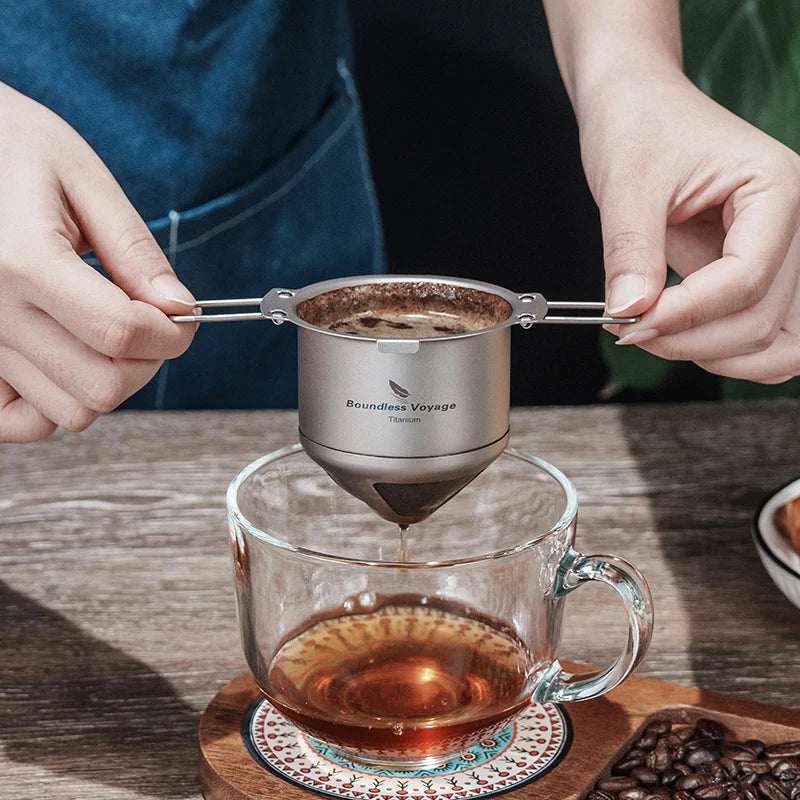 Person using a Titanium coffee filter to make tea in a glass mug on a wooden table.