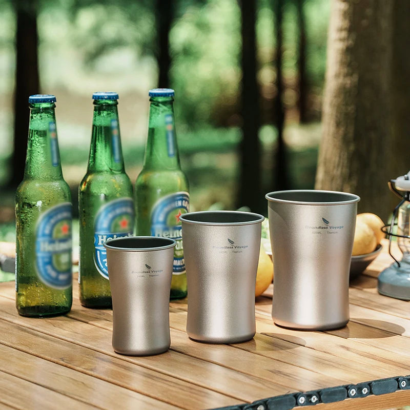 Metal cups and beer bottles on a wooden table with a forest background