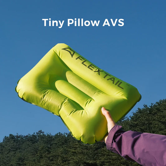 Yellow inflatable pillow labeled 'FLEXTAIL' held by a person against a blue sky with trees.
