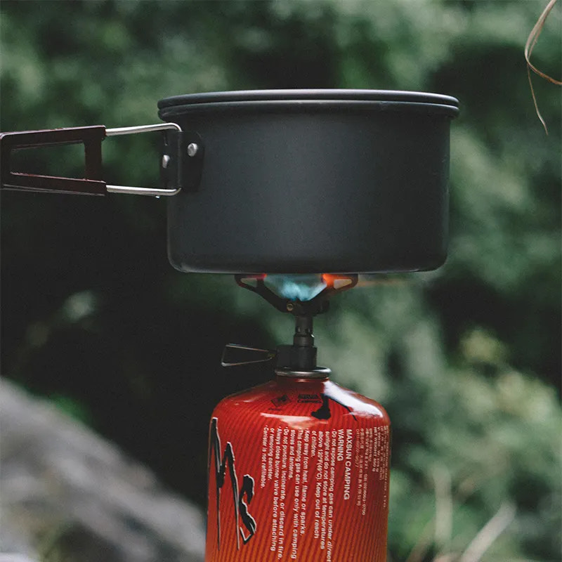 Black camping pot on a red gas canister with a blurred green background